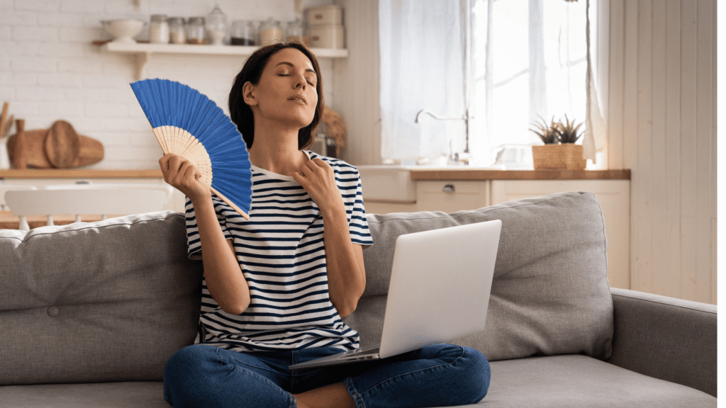 Woman sitting in the living room with a fan to cool herself down since the air conditioning is no longer working properly